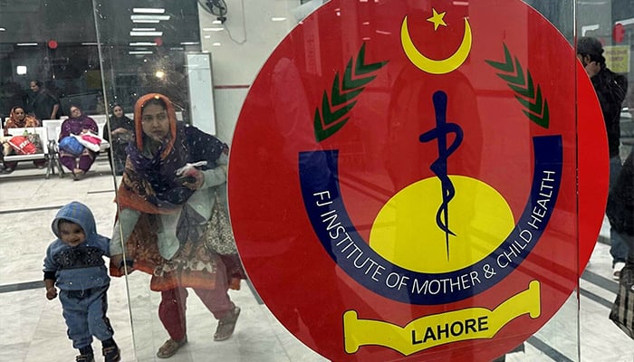 A woman with a child enters the mother and child unit of a teaching hospital, which is experiencing an influx of patients suffering from respiratory illness due to rising air pollution in Lahore on December 4, 2023. — Reuters