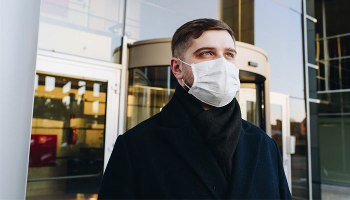 A man stands outside a building with a mask on. — Unsplash