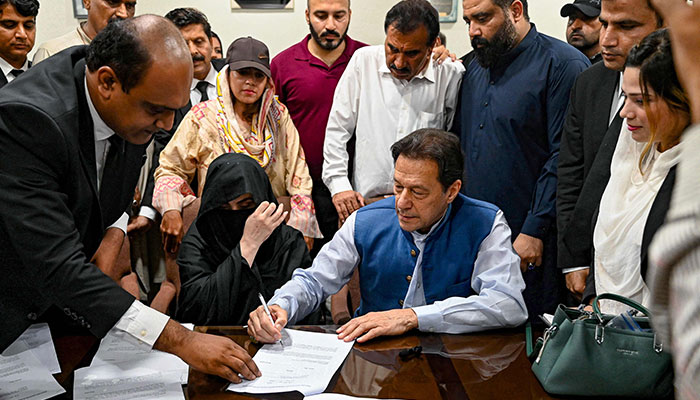 Pakistan´s former Prime Minister, Imran Khan (C) along with his wife Bushra Bibi (C, left) signs surety bonds for bail in various cases, at a registrar office in the High court, in Lahore on July 17, 2023. — AFP