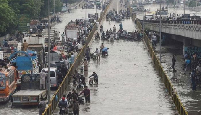 Commuters cross a flooded street after heavy rainfall in Karachi. — AFP/File