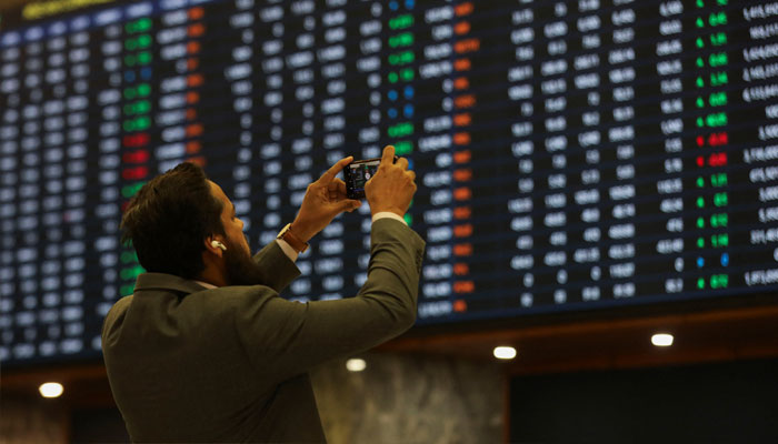 A man uses a mobile phone as he takes a photo of the electronic board displaying share prices during a trading session at the Pakistan Stock Exchange, in Karachi, Pakistan November 28, 2023. —Reuters