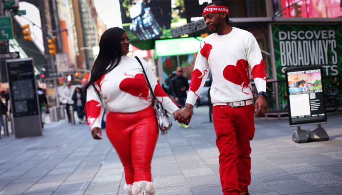 A couple wearing heart-themed sweaters walk hand in hand along Times Square on Valentine's Day in New York.  —Reuters