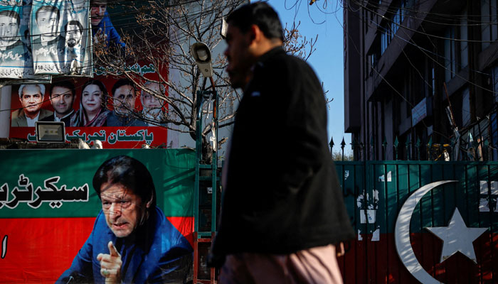 People walk past a banner with a picture of the former prime minister Imran Khan outside the party office of Pakistan Tehreek-e-Insaf (PTI), a day after the general election, in Lahore. —Reuters/File