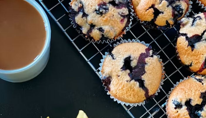 This image shows blueberry muffins placed on a grill next to a cup of tea. — Unsplash