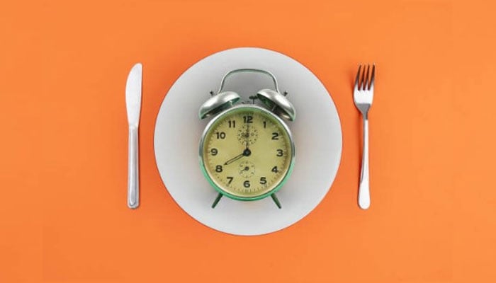 An alarm clock placed on a plate next to utensils representing the fasting-mimicking diet. — Pixabay