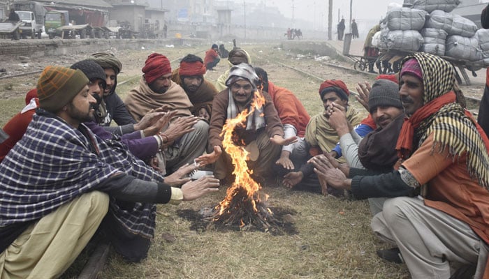 Coolies gather around a bonfire to warm themselves as cold weather grips Lahore on January 6, 2024. — Online