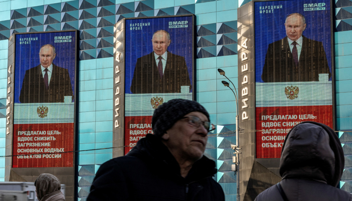 People wait for a bus next to electronic screens on the facade of a building showing an image of Russian President Vladimir Putin and a quote from his address to the Federal Assembly, in Moscow, Russia, February 29, 2024. — Reuters