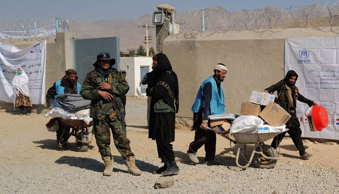 UNHCR workers push wheelbarrows loaded with aid supplies for displaced Afghan families as a Taliban fighter secures the area outside the distribution center on the outskirts of Kabul, Afghanistan October 28, 2021. — Reuters