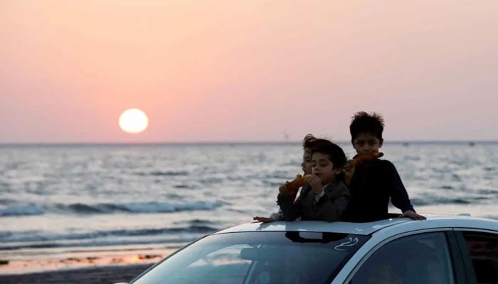 Children eat corn on cob as they ride on a car against the setting sun on New Years Eve in Karachi on December 31, 2022. — Reuters