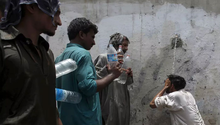 A man cools off under a public tap, while others wait to fill their bottles, during intense hot weather in Karachi. — Reuters/File