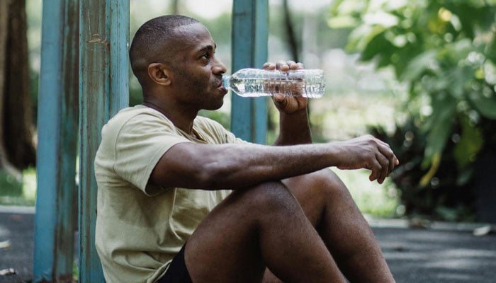 This representational image shows a man drinking water from a plastic bottle. — Pexels
