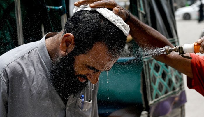 A volunteer sprays water on a bypasser´s face to cool off during a hot summer day along a street in Karachi on June 24, 2024. — AFP