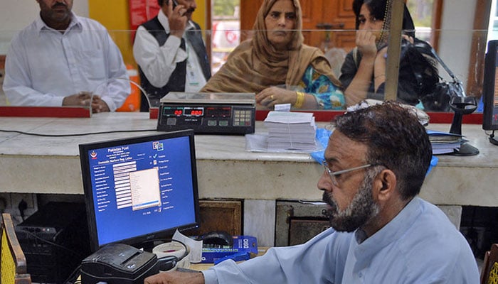 A Pakistani Post office employee enters mail addresses into a computer database as customers look on in Islamabad, Pakistan, on September 12, 2013. — AFP