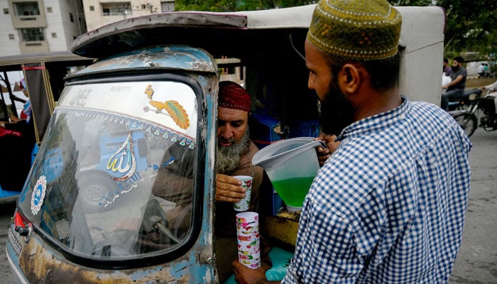A man serves cold drinks to commuters along a street on a hot summer day in Karachi on June 27, 2024. — AFP