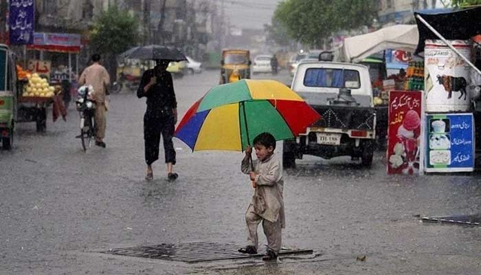 بارش کے دوران سڑک پر چلتے ہوئے ایک بچہ چھتری اٹھائے ہوئے ہے۔  — اے ایف پی/فائل