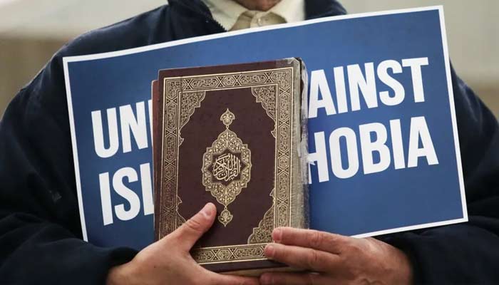 A representational image depicting a man holding Holy Quran and a placard reading united against Islamophobia. — Reuters/File