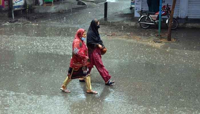 Women on their way on a road during heavy rain on March 24, 2023. — Online