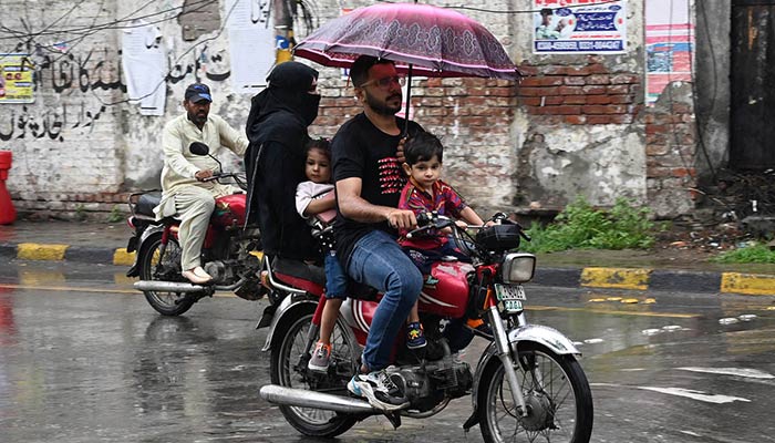 A man shields his family from the rain with an umbrella while riding a motorcycle in the Lahore on July 6, 2024. — AFP