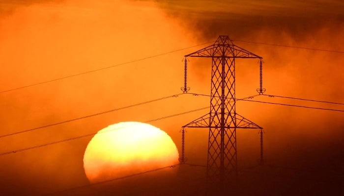 The sun sets behind an electricity pylon, as fog develops, on December 1, 2022. — Reuters