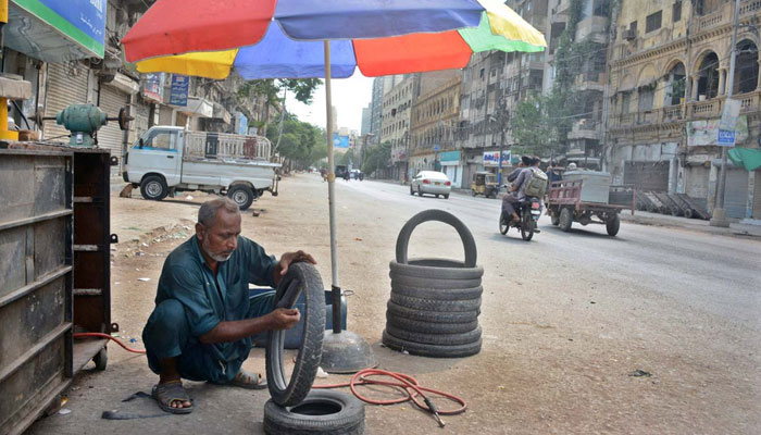 A mechanic busy in repairing puncture tyre of motorcycle under shadow of umbrella during scorching hot weather in Karachi on June 30. — APP