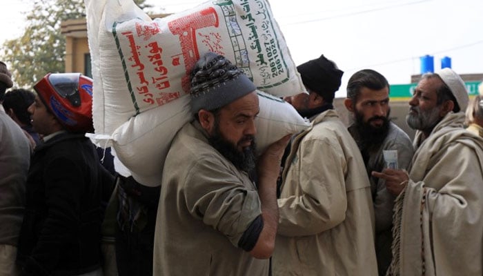 A man carries sacks of flour on his shoulder, while others stand in queue to purchase from a truck along a road in Peshawar, Pakistan January 20, 2020. — Reuters