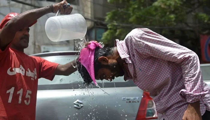 A volunteer pours water on a pedestrian along a street during a hot summer day in Karachi. — AFP/File