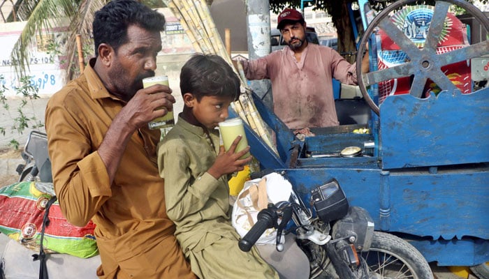 A man and his son beat the heat with traditional sugarcane juice while sitting on their bike in Karachi on July 1, 2024. — .APP