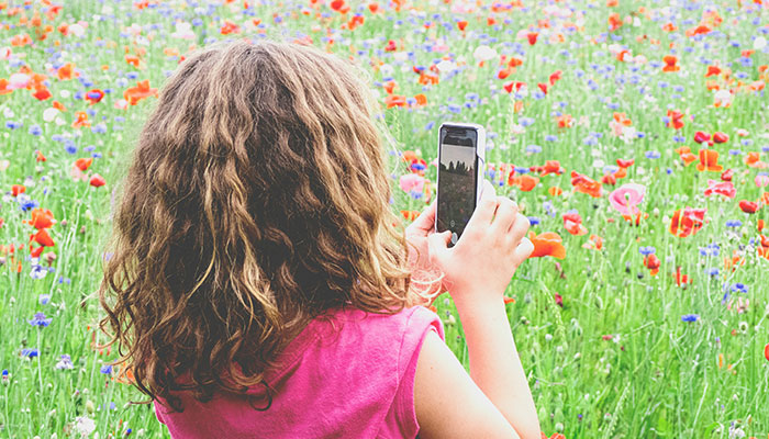 A child capturing pictures in the field using a smart phone. — Unsplash/File