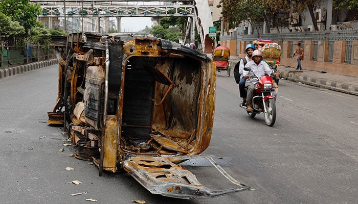 Men ride on a motorbike past a damaged vehicle that was set afire by a mob during clashes after violence erupted following protests by students against government job quotas, in Dhaka, Bangladesh, July 22, 2024. — Reuters