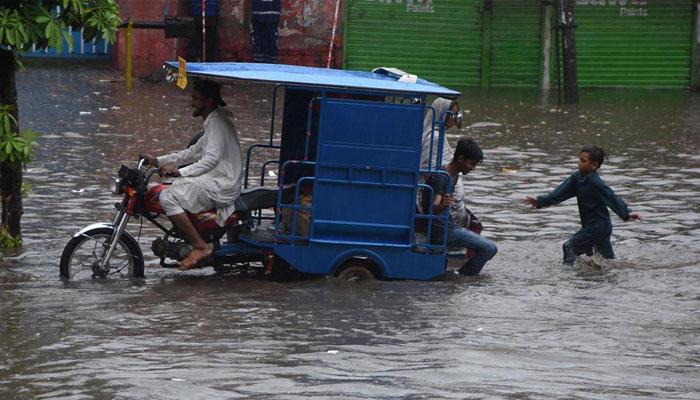 People can be seen passing through accumulated water on a road during rain in Lahore on July 12. 2024. — APP