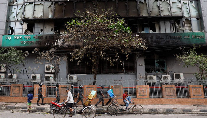 Security personnel and rickshaw pullers move past a partially damaged government building, that was set afire by a mob during clashes after violence erupted following protests by students against government job quotas, in Dhaka, Bangladesh, July 22, 2024. — Reuters