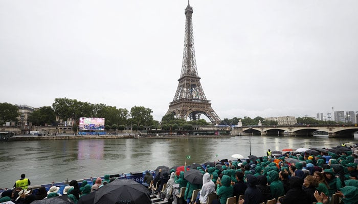 Spectators sat with umbrellas in front of the Eiffel Tower during the opening ceremony. — Reuters