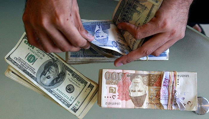 A currency dealer counts Pakistani rupees and U.S. dollars at his shop in Karachi. — Reuters/File