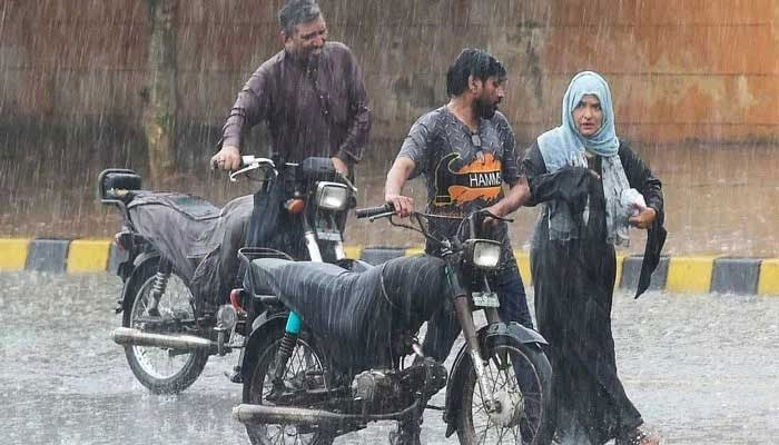 Commuters push their motorbikes along a street during a monsoon rainfall in Karachi on July 5, 2022. — AFP