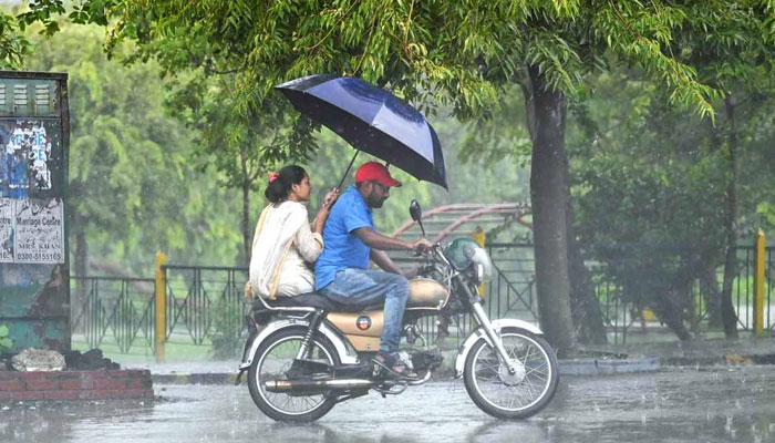 A man and a woman take a ride on a motorbike seeking cover under an umbrella from heavy rainfall in Islamabad on July 23, 2024. — APP