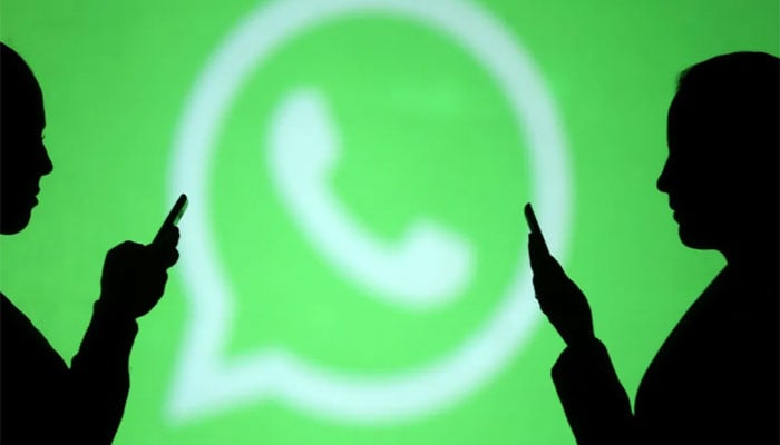 WhatsApp logo pictured with two people standing in front of it. — Reuters/File