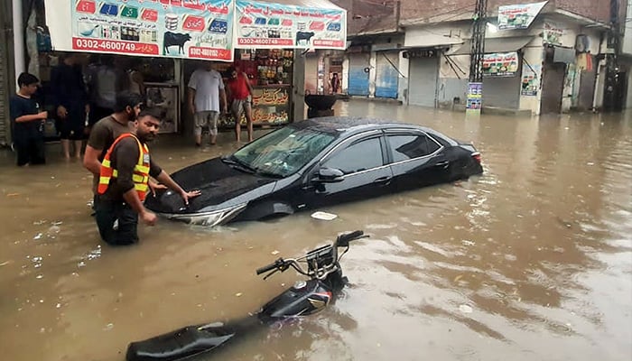 Rescue workers push a stuck car from the floodwater after a drain system failure during historic rains that broke a 44-year record in Lahore on August 1, 2024. — APP