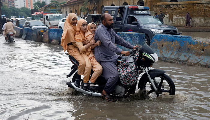 A man and students ride on a motorcycle on a flooded road, following rains during the monsoon season in Karachi, August 10, 2022. — Reuters