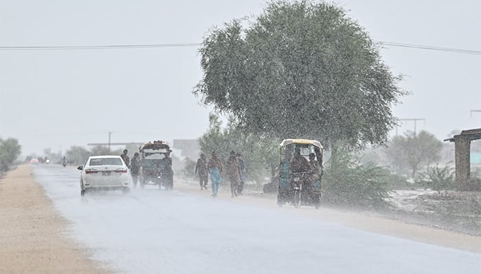 Commuters make their way along a street during rainfall on the outskirts Dadu on August 4, 2024. — AFP