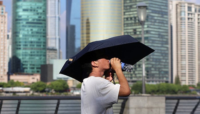 A man drinks from a water bottle under an umbrella as he walks amid a red alert for heatwave,in Shanghai, China, on August 1, 2024. — Reuters