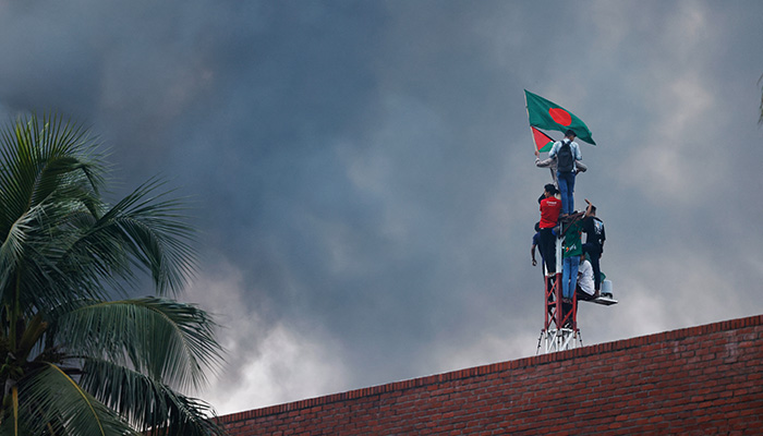 People wave a Bangladesh flag as they climb a structure at Ganabhaban, the Prime Ministers residence, after the resignation of the Sheikh Hasina in Dhaka, Bangladesh, August 5, 2024. — Reuters