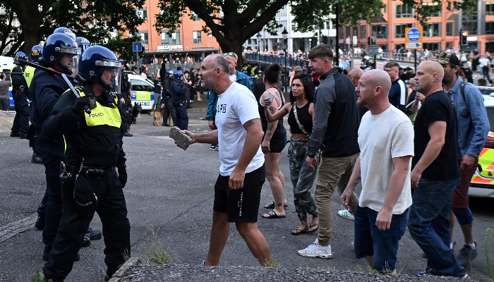 A protester holding a piece of concrete walks towards riot police as clashes erupt in Bristol on August 3, 2024. —AFP