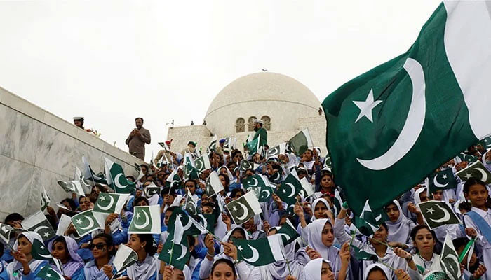 Attendees wave Pakistan’s national flag while singing national songs at a ceremony to celebrate the country’s Independence Day at the mausoleum of Muhammad Ali Jinnah in Karachi. — Reuters/File