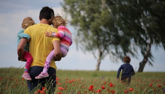 A man holding two children in a windy field. — Unsplash/File