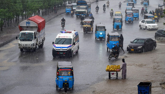 People wade through a flooded street amid rainfall in Karachi on July 30, 2024. — AFP