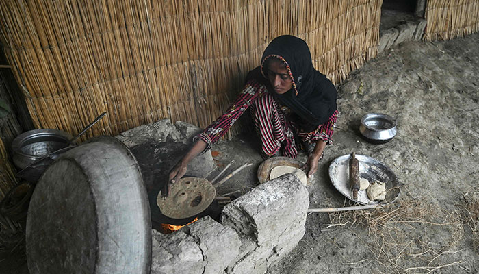 Najma Ali, a monsoon bride who was married underage, prepares flatbread outside her hut at Khan Muhammad Mallah village in Dadu district on August 3, 2024. – AFP