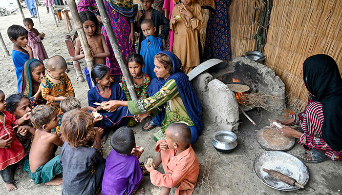 Hakim Zaadi (C), village matron and mother of Najma Ali (R), a monsoon bride who was married underage, distributes flatbread to children outside her hut at Khan Muhammad Mallah village in Dadu district on August 3, 2024. – AFP