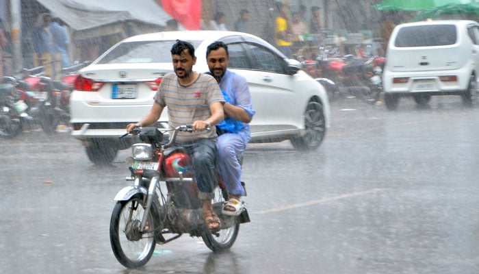 Two men on a bike ride through rain in Faisalabad on August 16, 2024. — Online