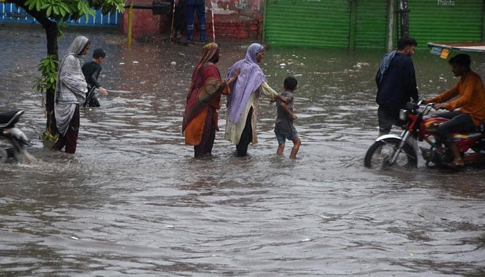 People passing through accumulated water on the road during rain in Lahore. — APP