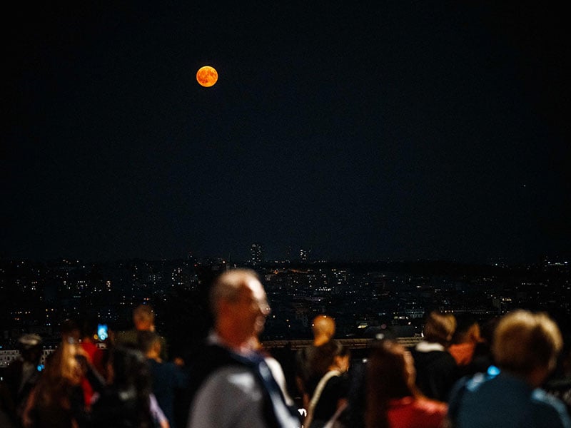 People watch the moon rising over Paris, on August 19, 2024. — AFP